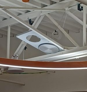An old clock/speaker combination meant for a wall that has had its clock removed and its speaker cannibalized for use in the cafeteria ceiling. Instead of screws, it has been fastened to a beam with safety wire. 
