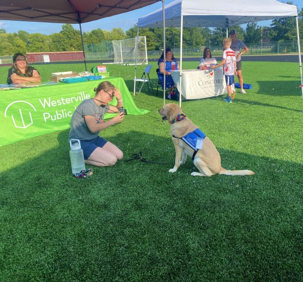 South’s social worker and Hope Squad advisor, Noelle Spriestersbach, kneels to take photos of Twinkle, the school’s facility dog. In the back, Annamarie Carlson, youth services manager at Westerville Public Library runs a booth where people could receive free books, bookmarks, pens, and fidgets, which also featured fun bubbles.