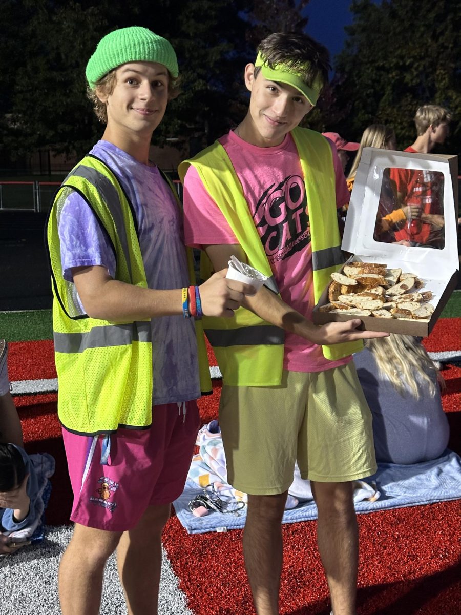 Seniors Aiden Evans and Fletcher Fox handing out bagels in the morning for senior sunrise ending homecoming week with bright neon colors.